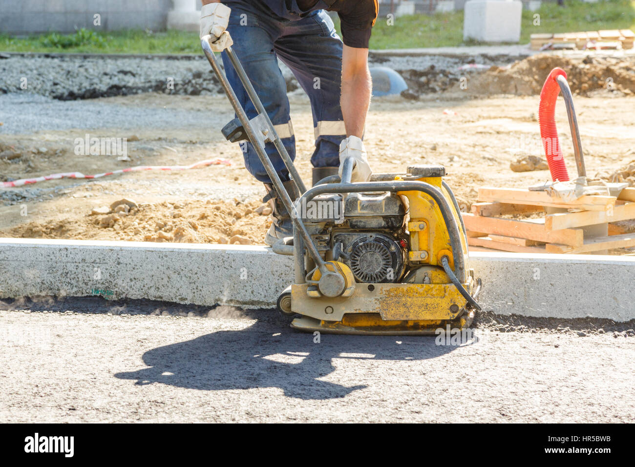 Worker use vibratory plate compactor compacting asphalt at road repair