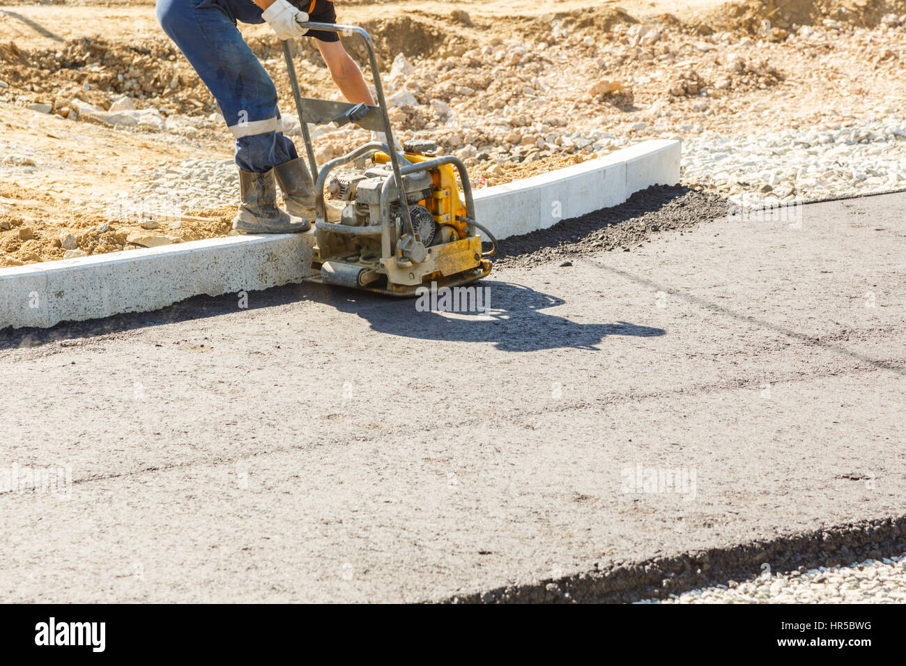 Worker use vibratory plate compactor compacting asphalt at road repair