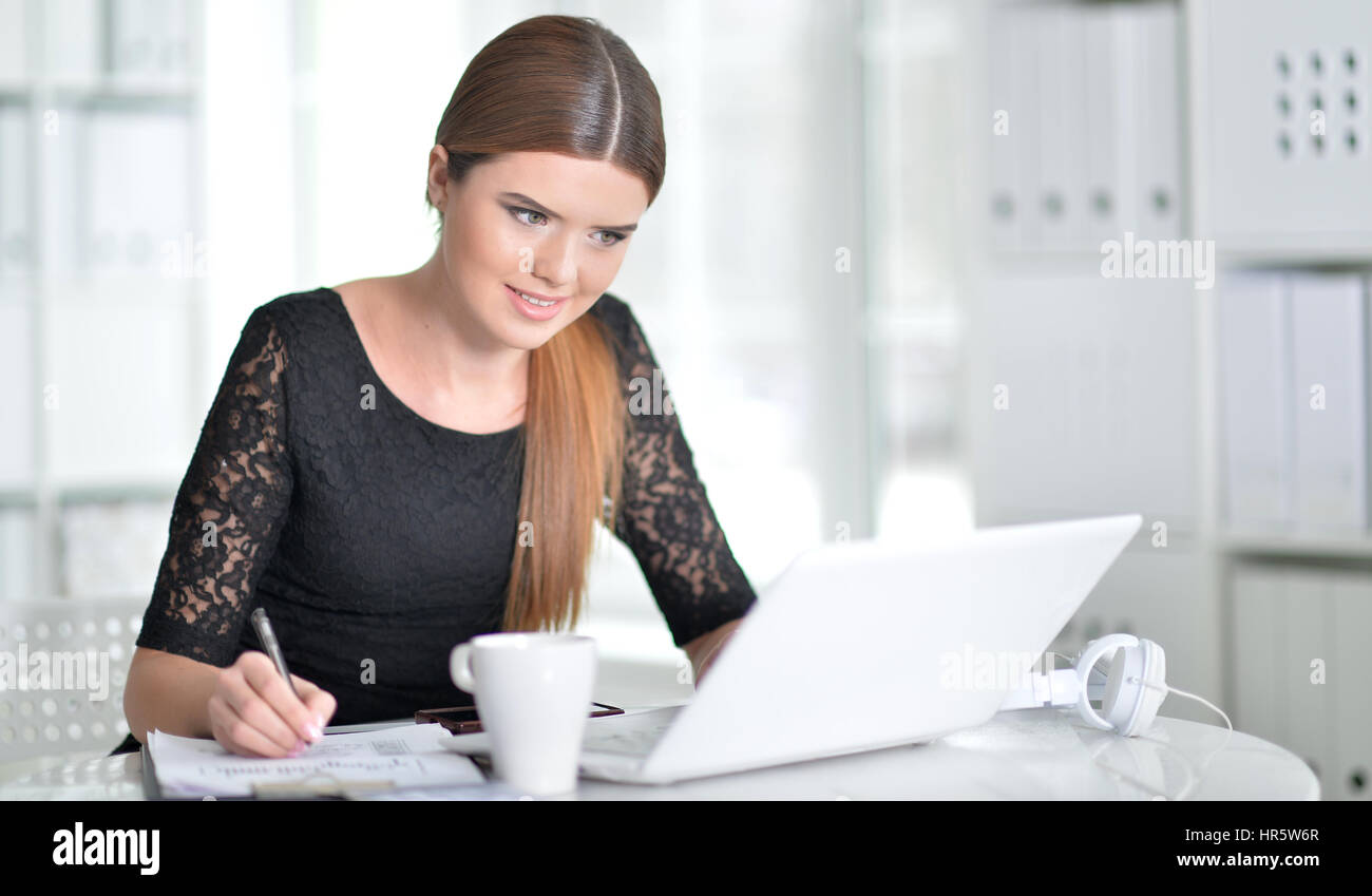 young woman making notes and using laptop Stock Photo