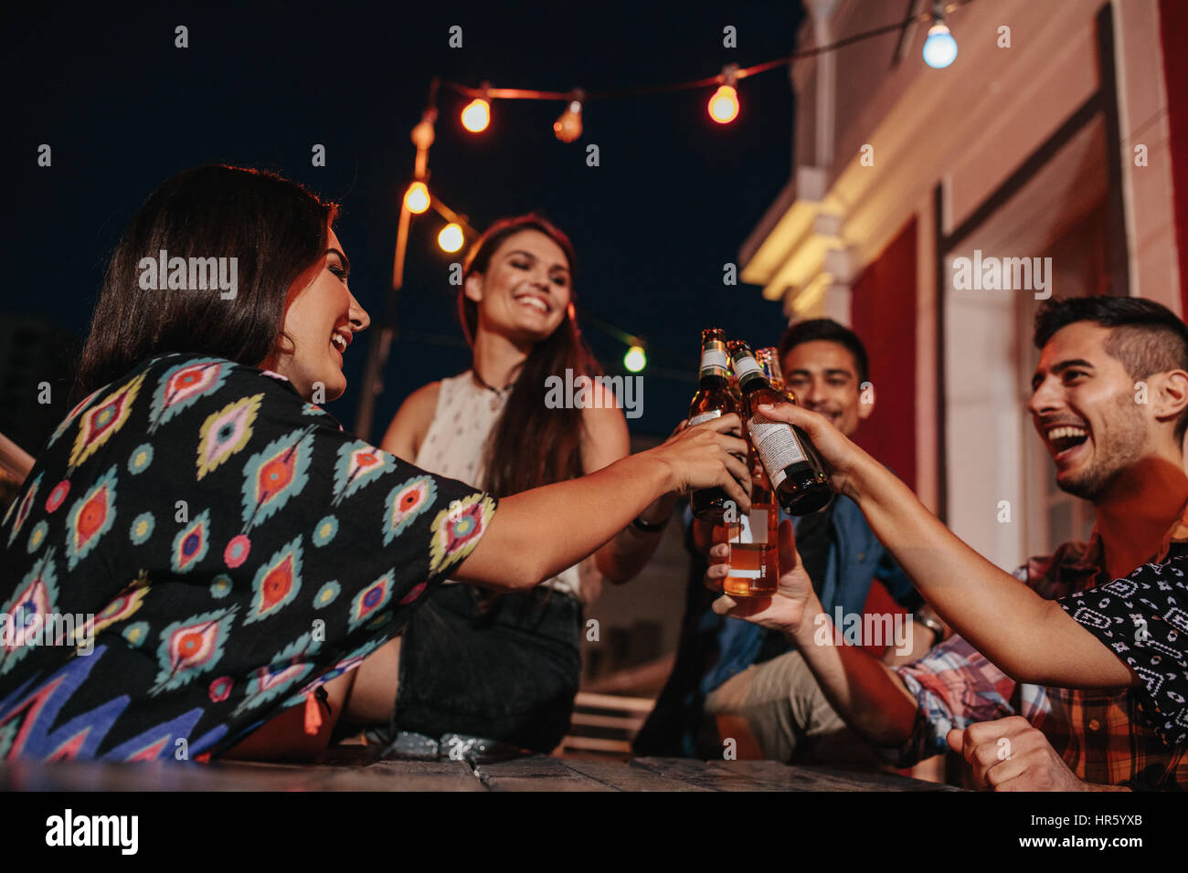 Group of young friends hanging out with drinks on rooftop. Young people at party toasting beers. Stock Photo