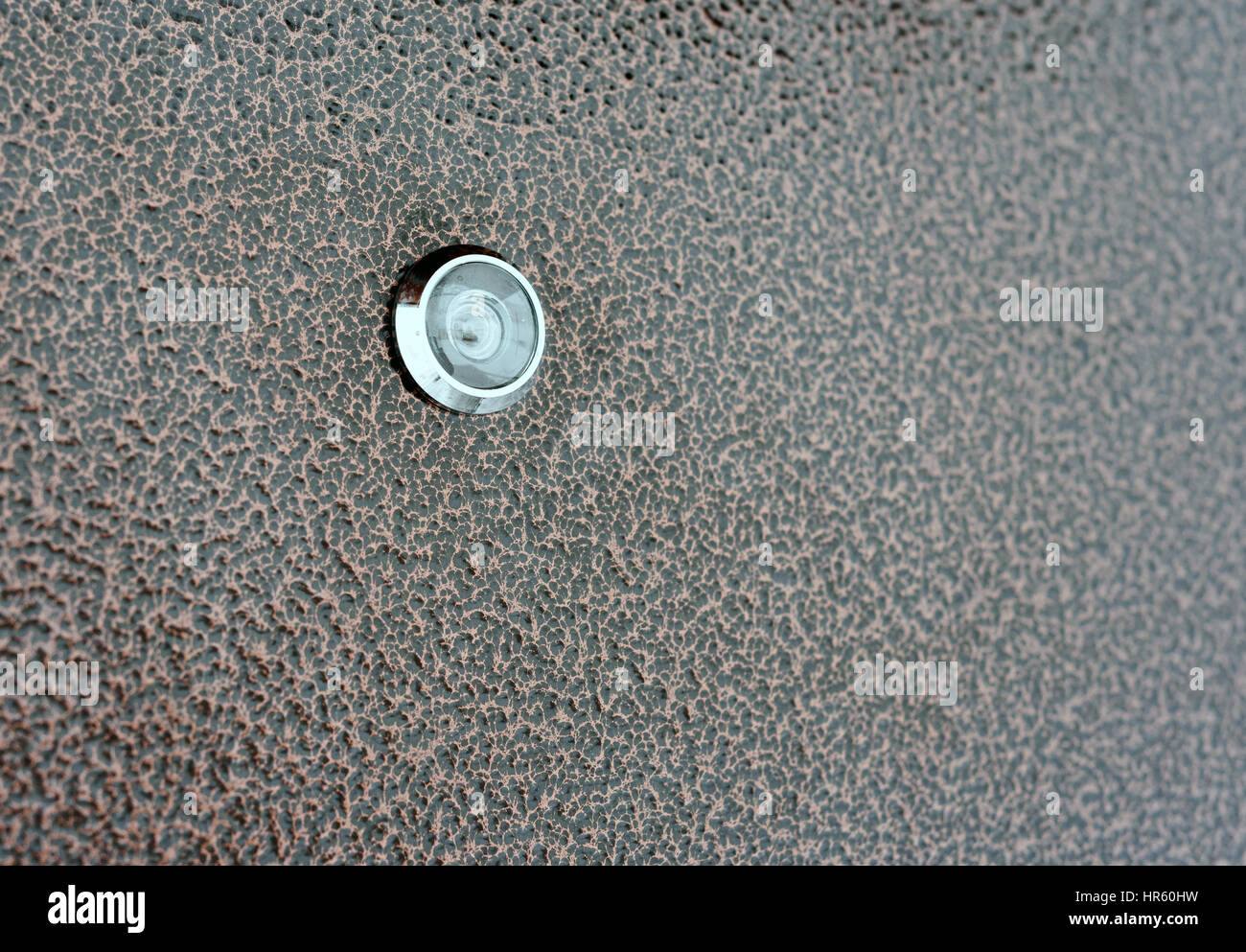 Single glass security peephole set against a brown metal house door Stock Photo