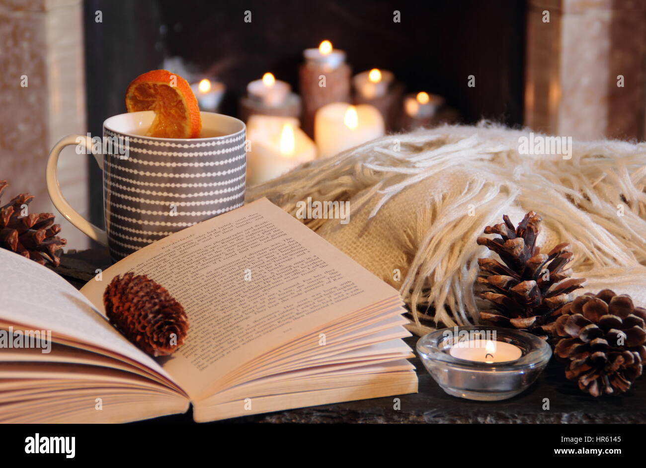 Reading by a candle lit open fireplace in a cosy English home with a mug of  hot tea and a blanket (throw) in autumn/early winter Stock Photo - Alamy