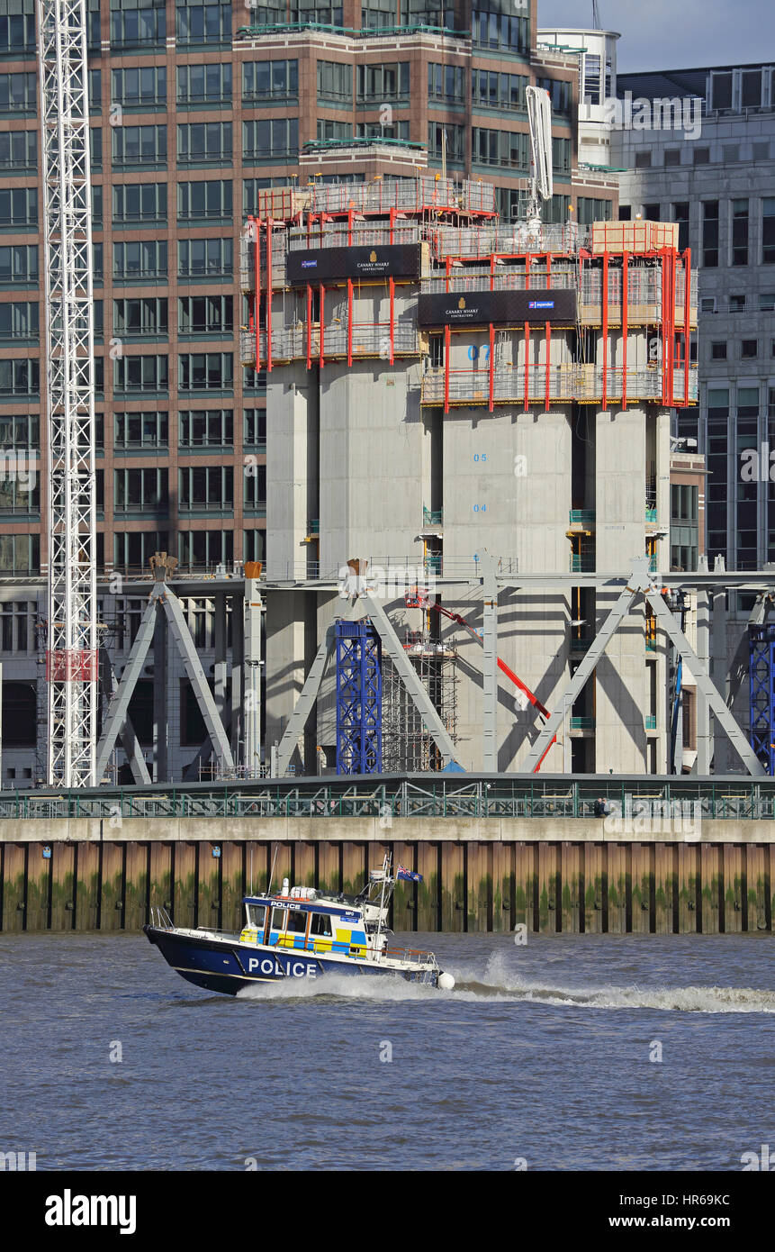 A police launch speeds along the River Thames in London, UK, passing a construction site at a Canary Wharf. Stock Photo