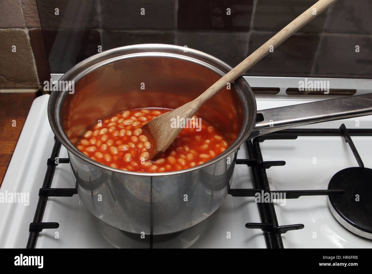 Saucepan of baked beans cooking on a gas oven hob with wooden spoon