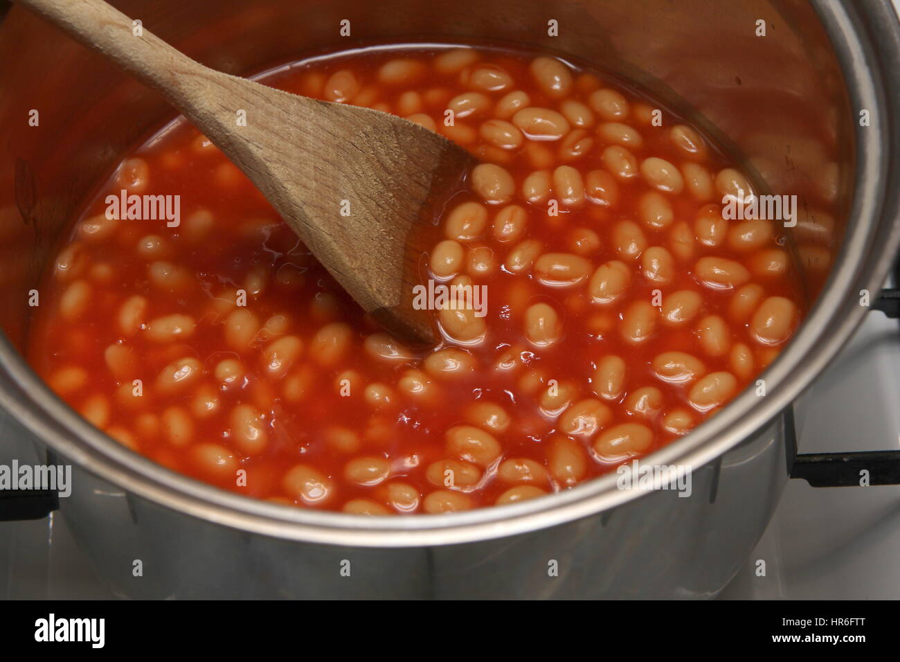 Saucepan of baked beans cooking on a gas oven hob with wooden spoon