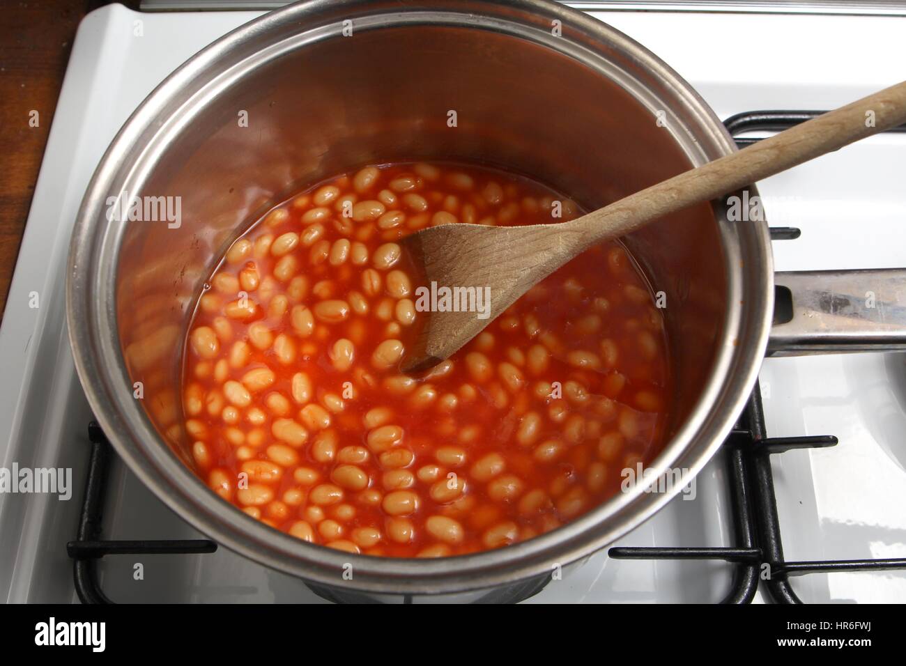 Saucepan of baked beans cooking on a gas oven hob with wooden spoon