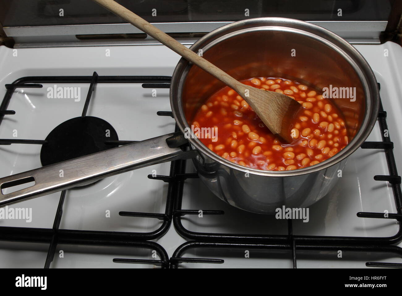 Saucepan of baked beans cooking on a gas oven hob with wooden spoon