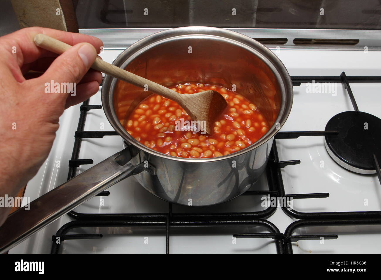 Man's hand stirring a pan of baked beans on a gas hob Stock Photo Alamy
