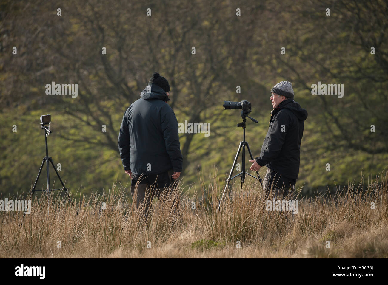 Their cameras on tripods, two male train spotters (enthusiasts) are chatting whilst for waiting for the next train - North Yorkshire, England. Stock Photo