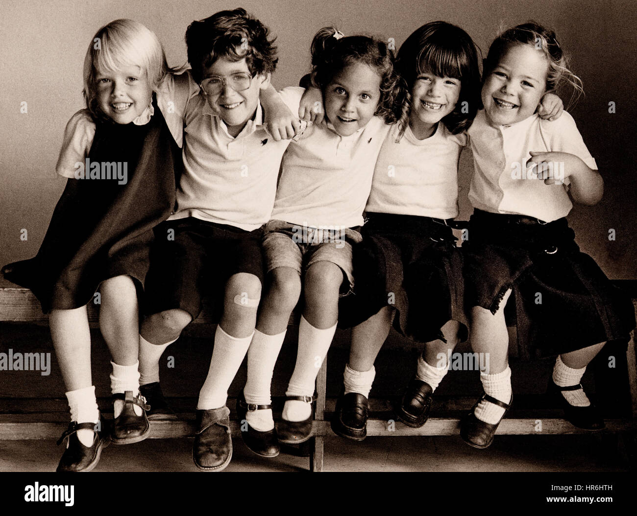 RETRO EDUCATION JUNIOR SCHOOL HAPPY NATURAL INFANT GROUP 5-7 years  3 girls and 1 boy smiling sitting on school bench, made for Kodak Art of 35mm Book. Image B&W Kodak Tri-X film study of primary school pupils sitting together on bench in natural light, enjoying being together and having an informal school photo taken..Ian Shaw Kodak Photographer Stock Photo