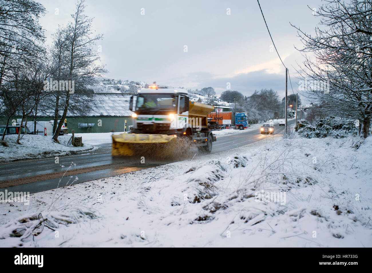 A snow plough clearing and gritting a rural village road snow covered in the village of Rhosesmor, Flintshire Stock Photo