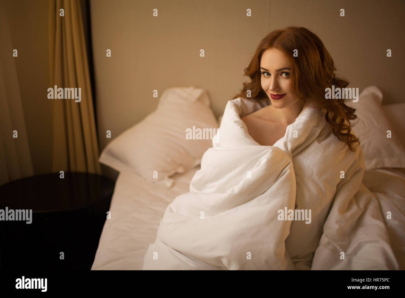 Red-haired girl covered herself with a blanket in the bed Stock Photo ...