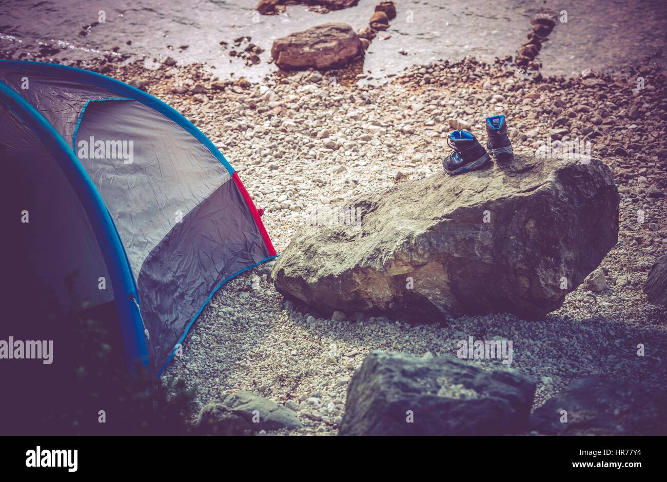 Lake Camping Scenery. Campsite on the Rocky Lake Shore. Outdoor and Recreation Theme. Wet Shoes on the Boulder. Stock Photo