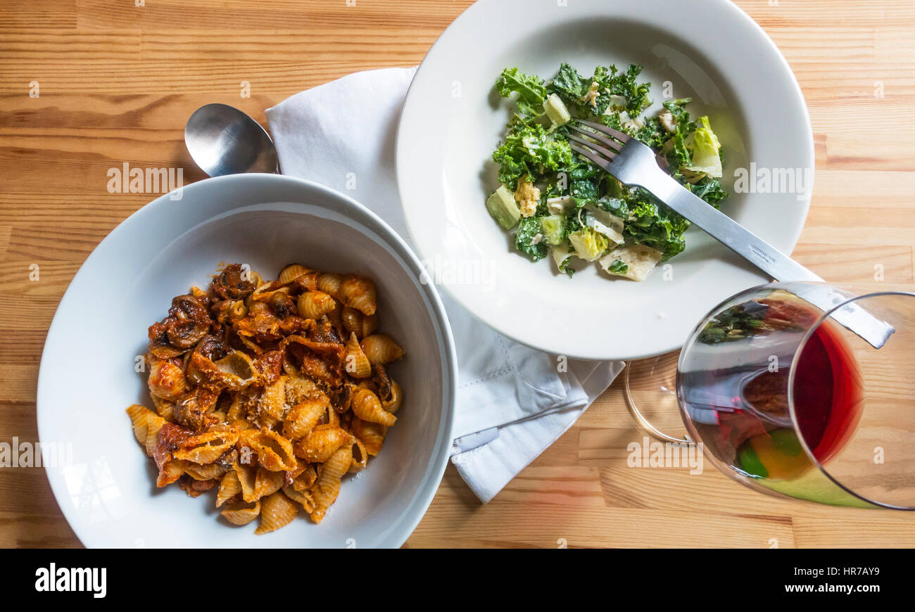 Pasta shells with bacon, mushrooms and tomatoes with a green salad and red wine Stock Photo