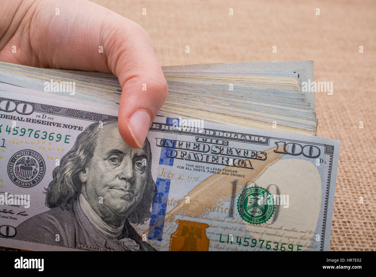 Hand holding banknote bundle of US dollar on a linen canvas background ...