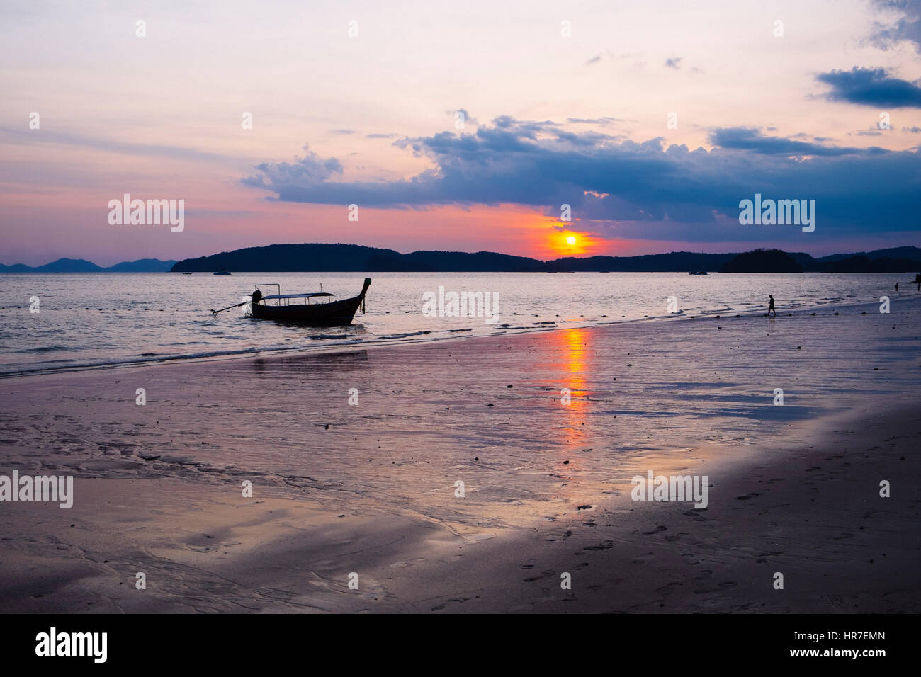 Two  distant human figures and a Thai long-tail boat at sunset, Ao Nang Beach, Krabi Province, Thailand Stock Photo
