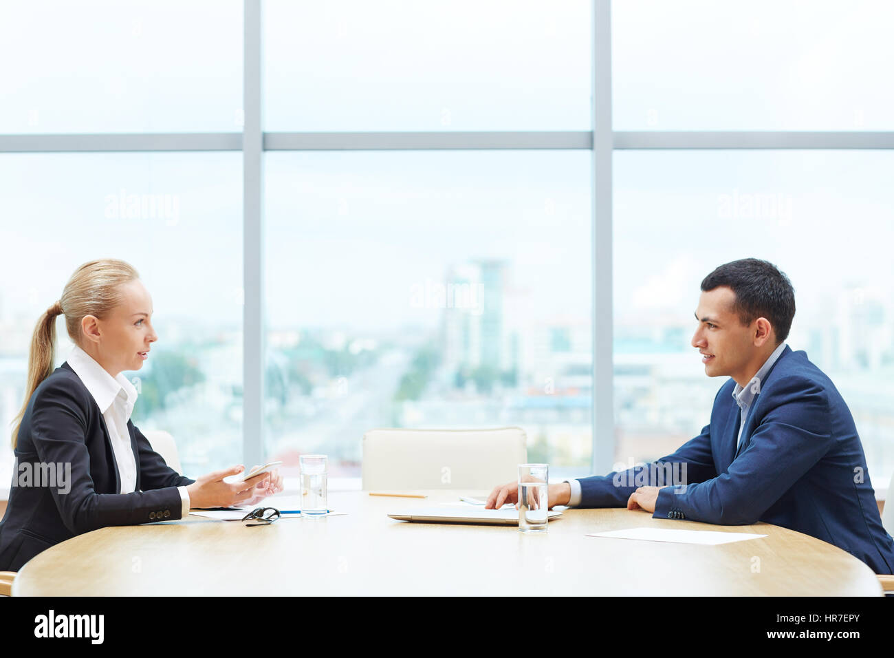 Profile view of two business people, man and woman,   representing sides of contract, sitting opposite each other at table discussing deal during meet Stock Photo