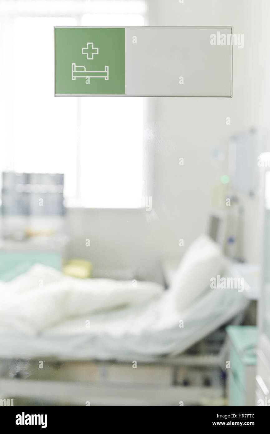 Image of empty bed in clinic with white clean sheets tossed over as if patient just got up and left, shot through glass door with green Hospital Ward  Stock Photo