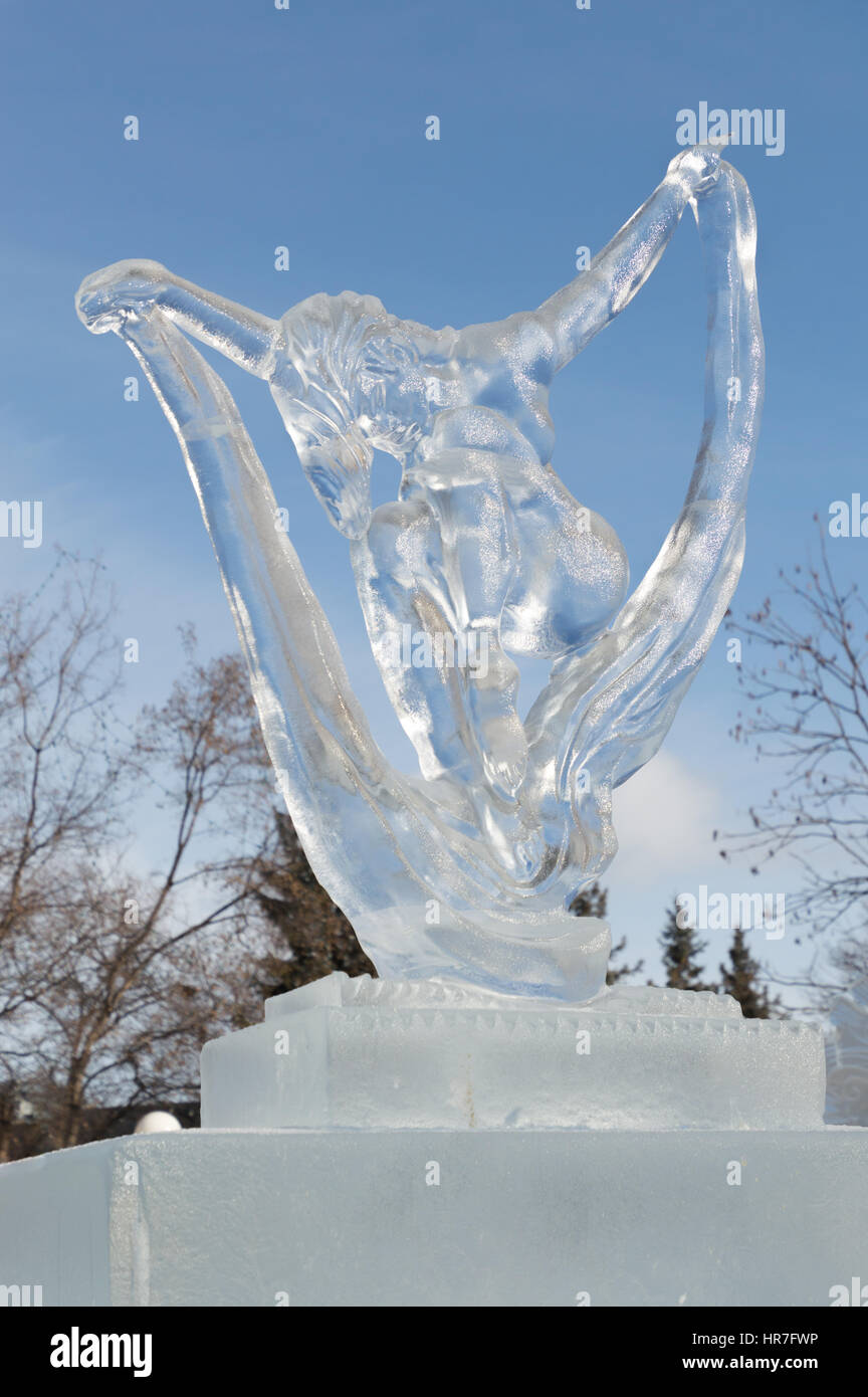 Ice sculpture in Ottawa, on a sunny day with trees behind. Ice carving shows a lady stretched with her arms up holding some ribbons Stock Photo