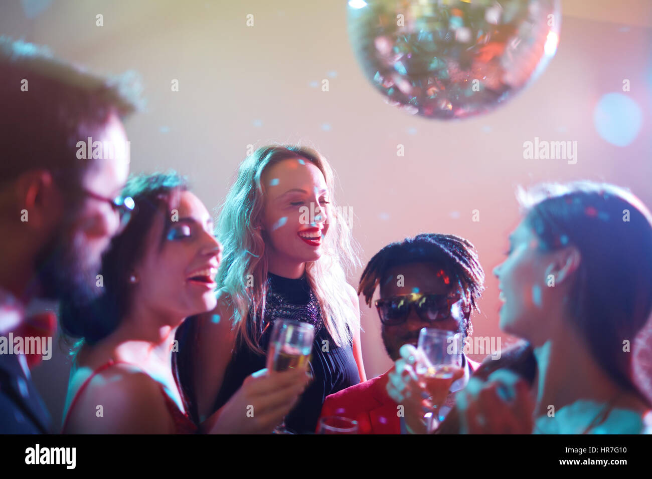 Dressy multiethnic group of friends gathered together and celebrating momentous event in nightclub, they laughing and drinking alcohol Stock Photo