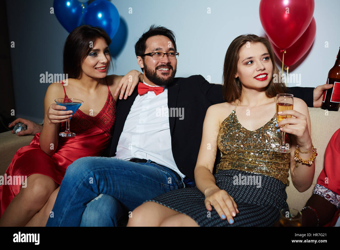 Male and female clubbers celebrating momentous event with alcohol: they sitting on couch and looking away joyfully Stock Photo
