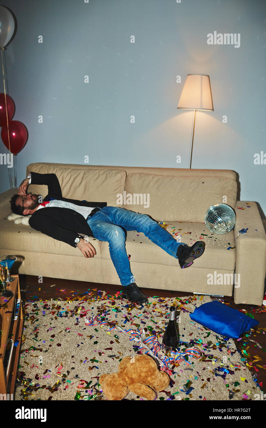 Messy room after wild party: colorful confetti thrown everywhere, empty alcohol bottles and champagne flutes standing on floor and coffee table, Asian Stock Photo
