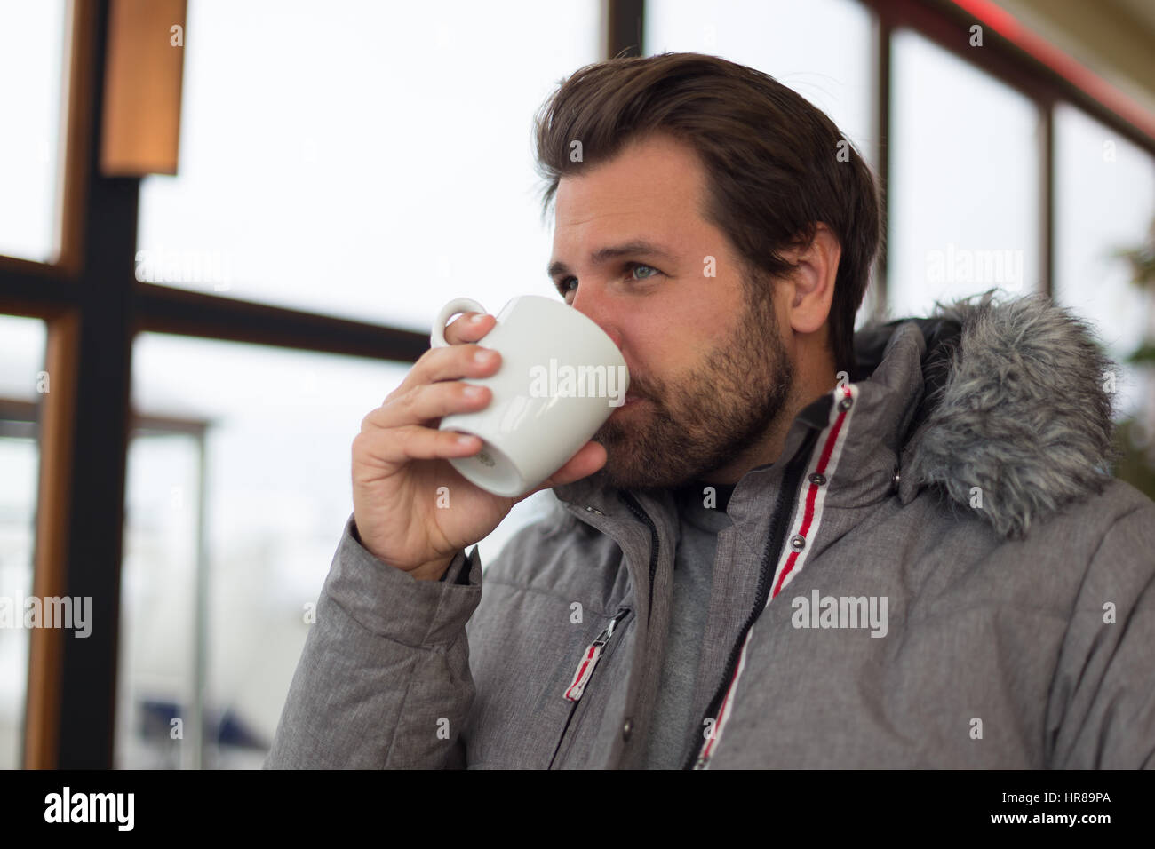 Thoughtful man wearing warm winter jacket looking out the window and drinking coffee. Stock Photo