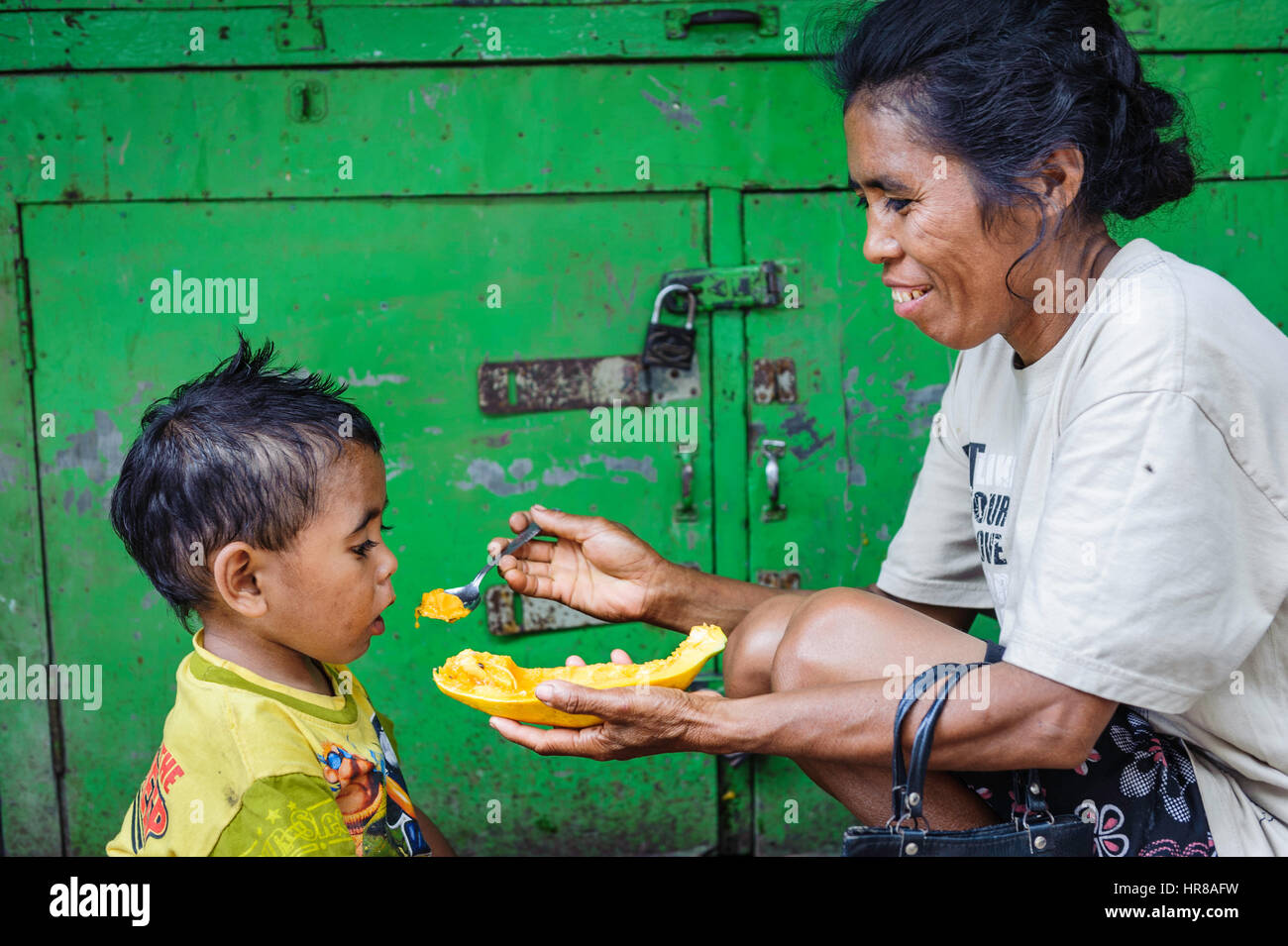 Woman feeding paw paw to her grandson in the street. Stock Photo