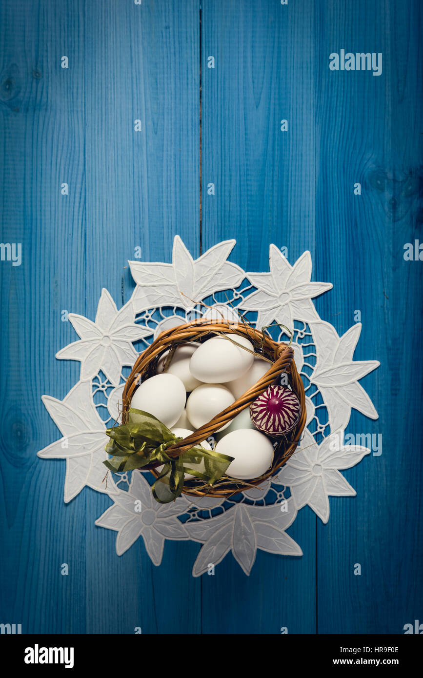 Group of eggs in wicker basket on the blue wooden surface. Easter concept. Stock Photo