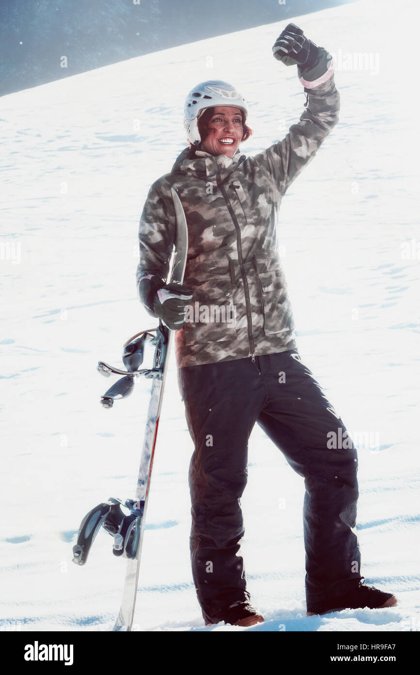 Smiling, red-haired woman with snowboarding on the slopes in winning pose. Stock Photo