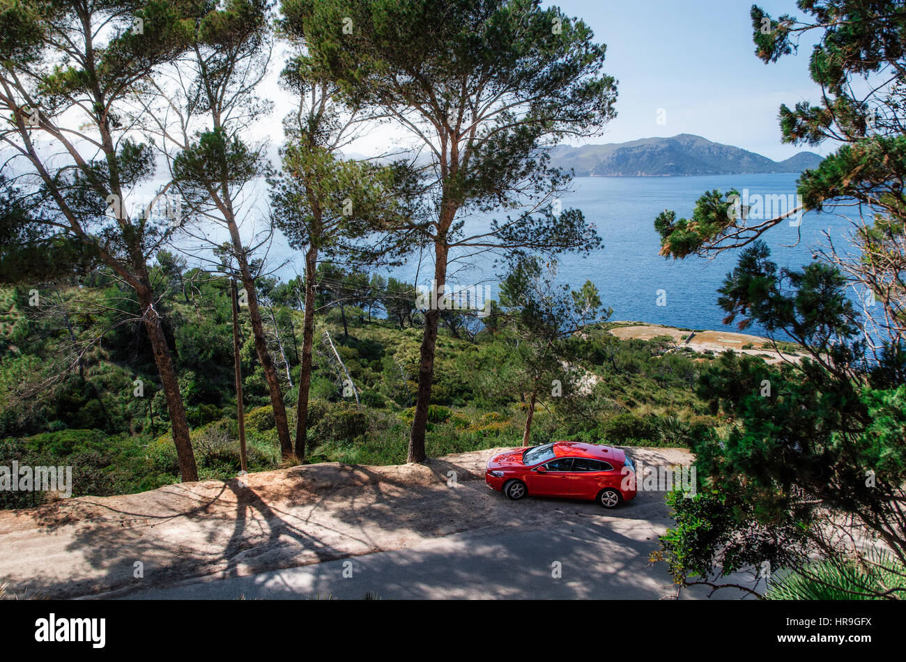 Alcudia, Mallorca, Spain - May 23, 2016: Seascape of Mediterranean Sea with a red car Volvo V40 traveling on the mountain serpentine through the pine  Stock Photo