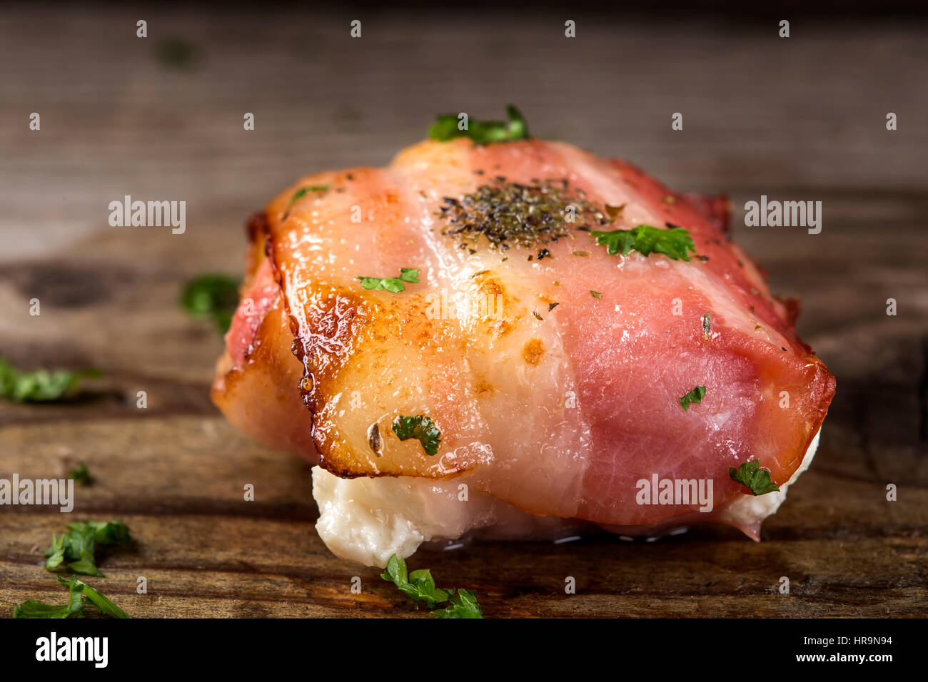 Close up of fried goat cheese wrapped in smoked bacon on wood with parsley Stock Photo