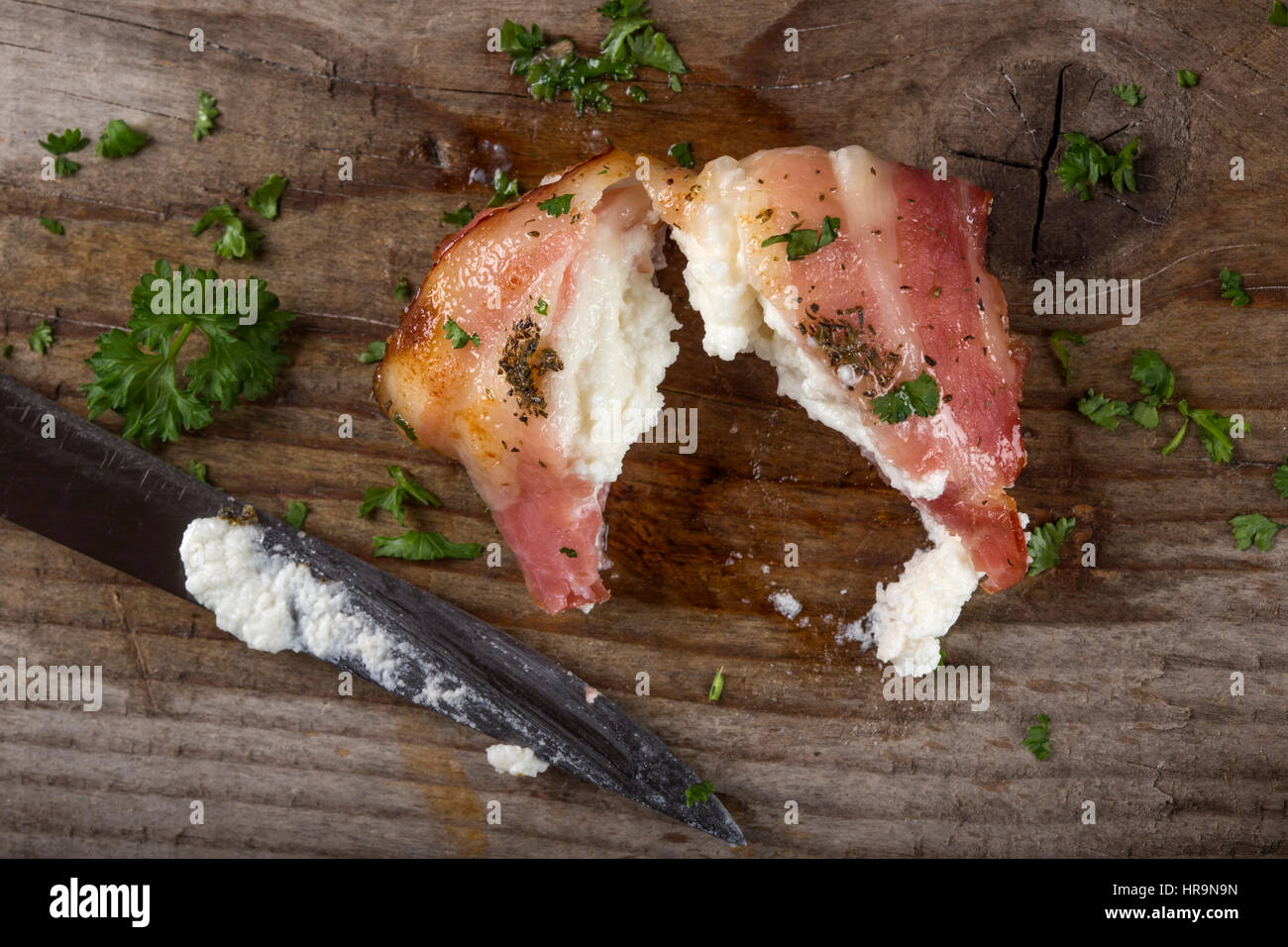 Fried goat cheese wrapped in smoked bacon on wood with knife and parsley Stock Photo
