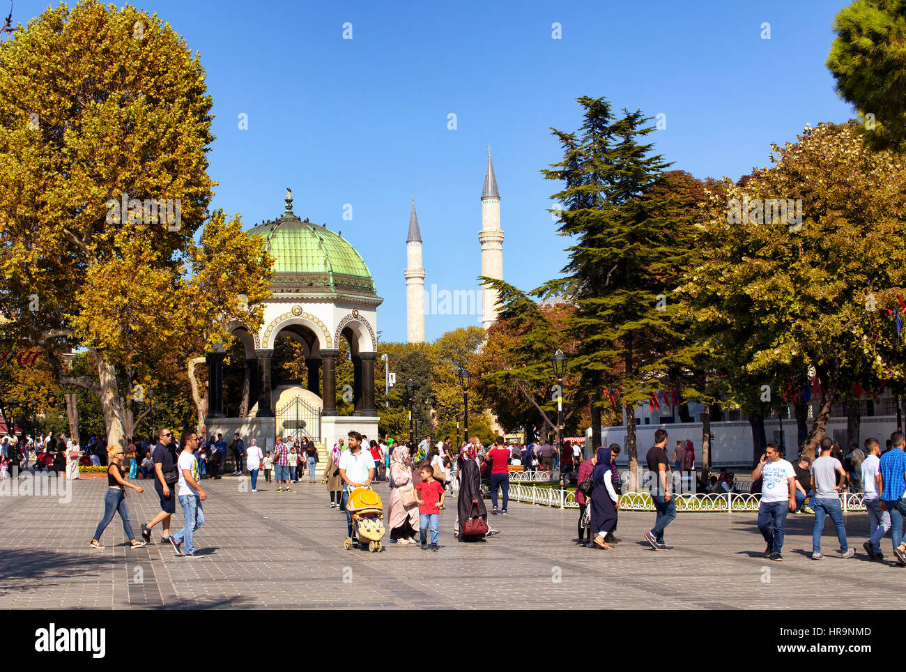 Local people and tourists walk around Sultanahmet area neat Blue Mosque in Istasnbul. German fountain and minarets of Blue Mosque are in the backgroun Stock Photo