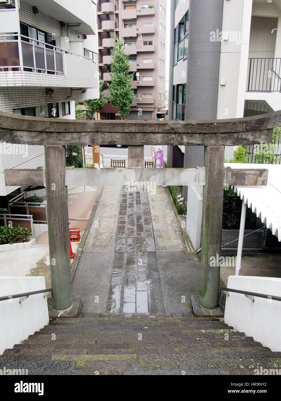 A torii gate between apartment buildings marks the entrance to a Shinto shrine in downtown Tokyo Japan. Stock Photo