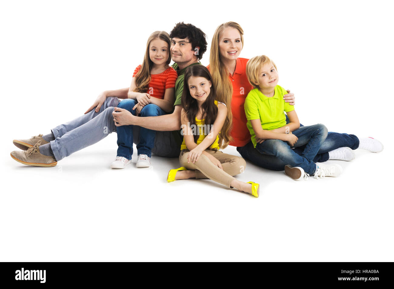 Portrait of happy family with three children sitting on the floor at studio isolated on white background Stock Photo