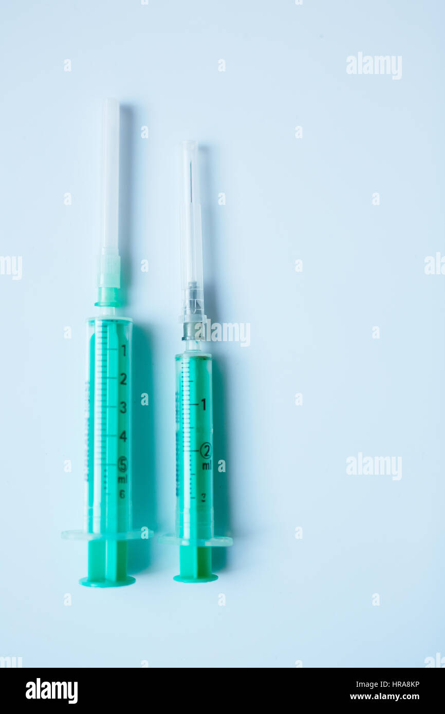 Two green plastic syringes of different sizes placed on white table