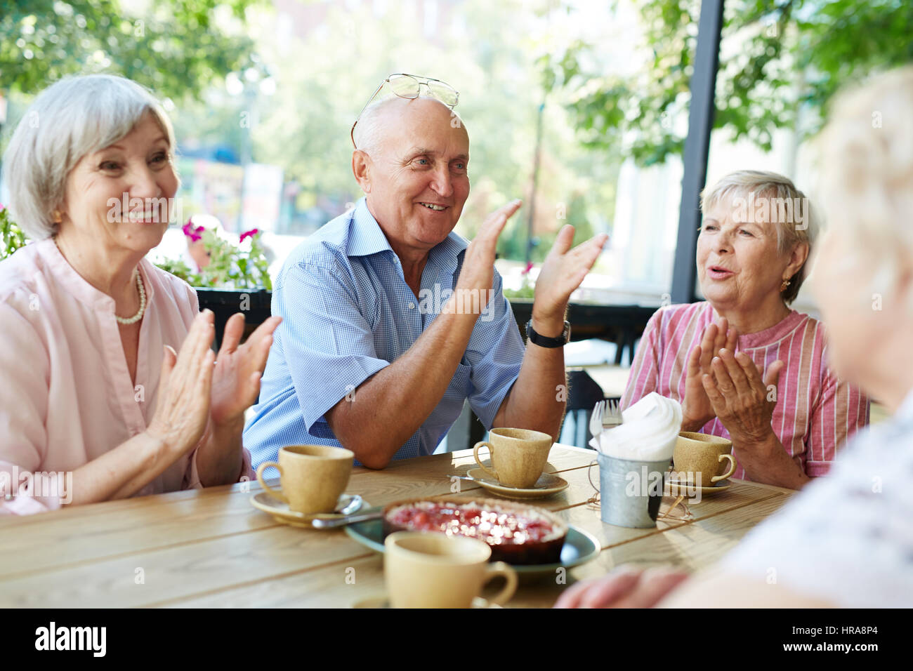 Group of smiling elderly people gathered together in outdoor cafe for