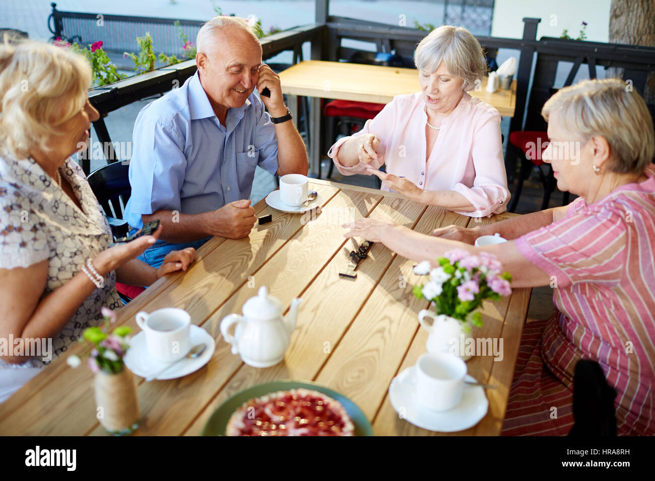 Smiling elderly people having tea party in lovely outdoor cafe and