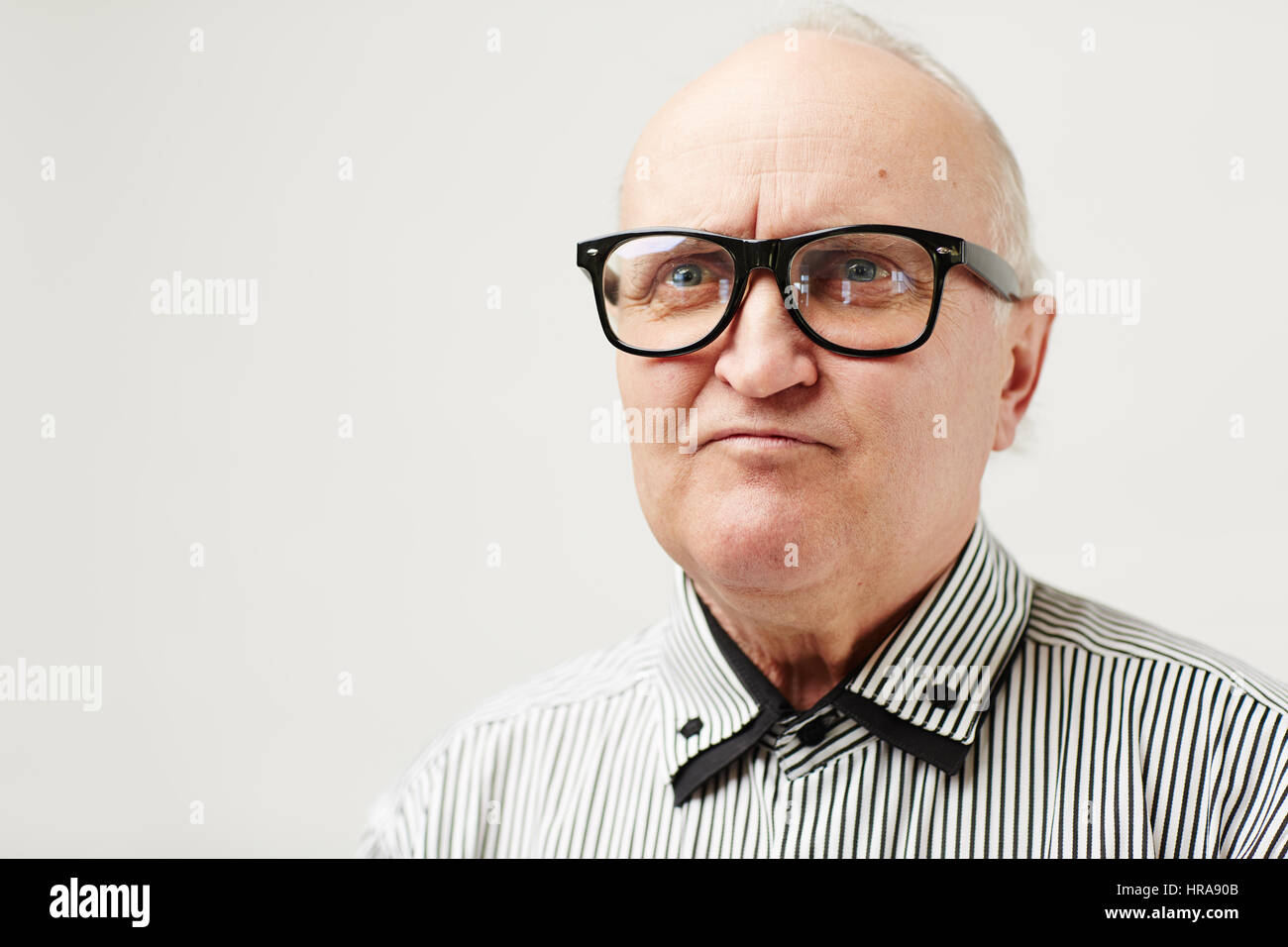 Portrait of funny male senior with receding hairline and eyeglasses looking to the side with pretended angry face expression Stock Photo