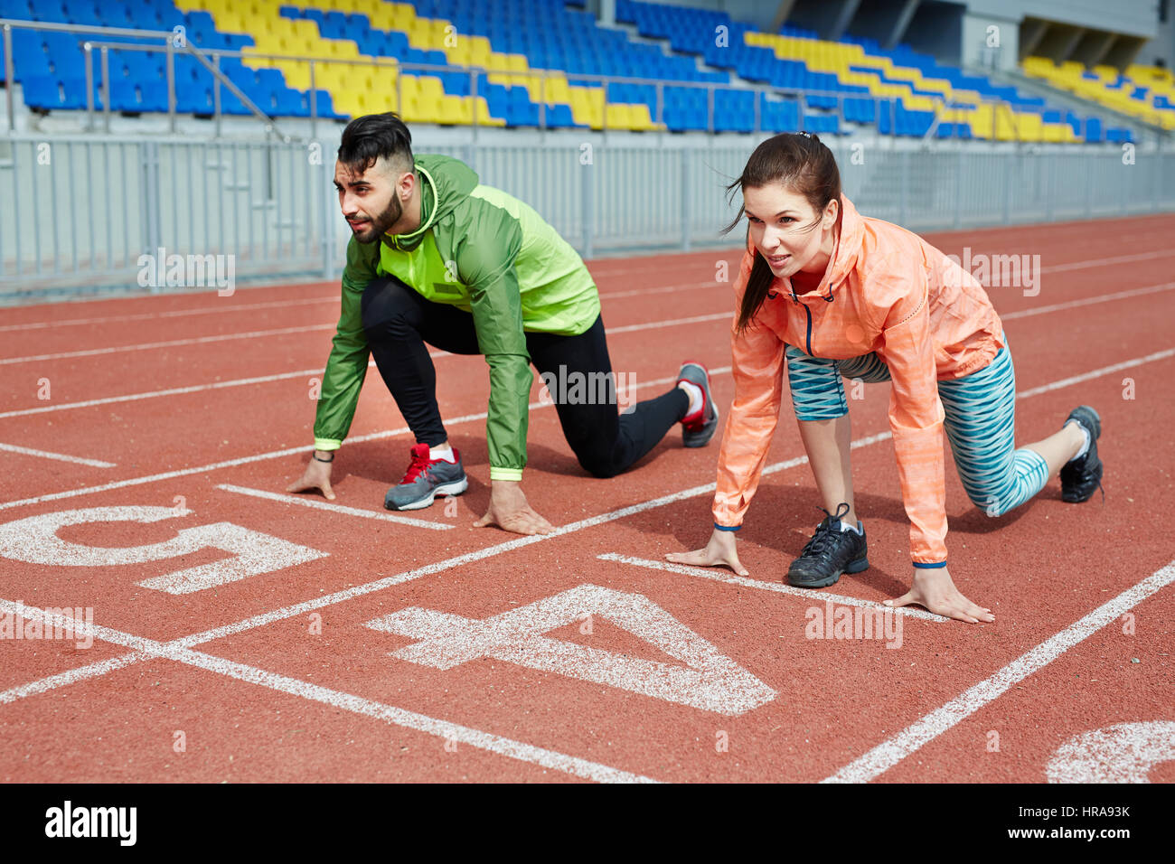 Couple of athletes, man and woman, standing close together on sprint tracks in stadium ready to start running competition Stock Photo