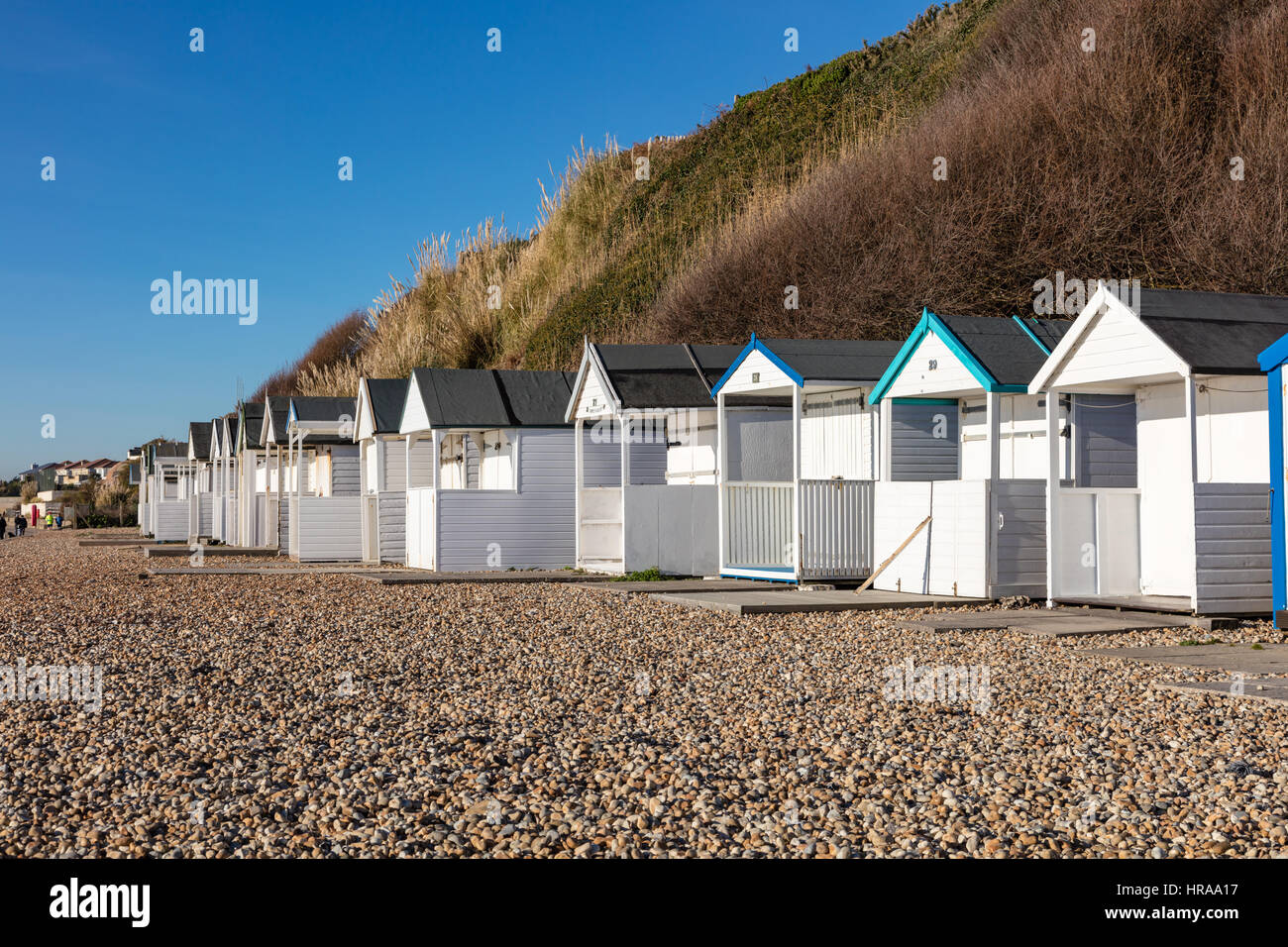 A row of beach huts under the cliffs at Bexhill, on the shingle beach under a blue sky, Bexhill on Sea, East Sussex, UK Stock Photo