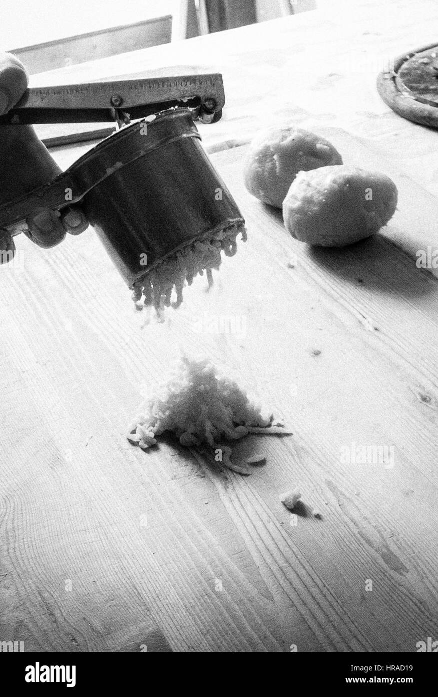 Hands using a potato ricer, preparing potato gnocchi in a rustic
