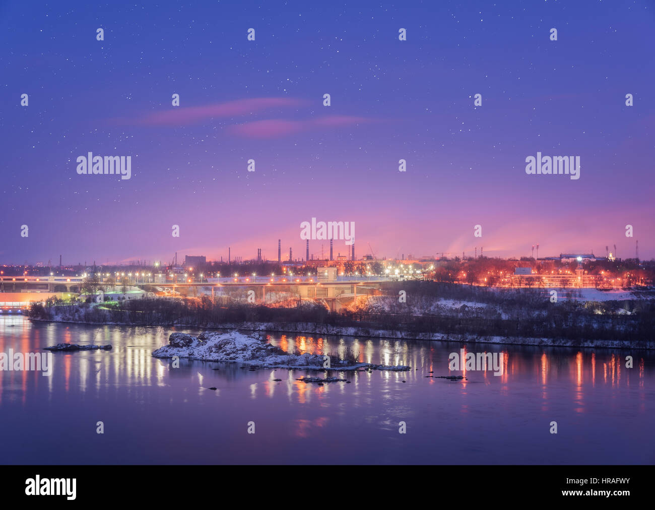 Night cityscape with colorful purple sky with stars, rocks, river, trees, buildings, city illumination and steel factory with smokestack in winter Stock Photo