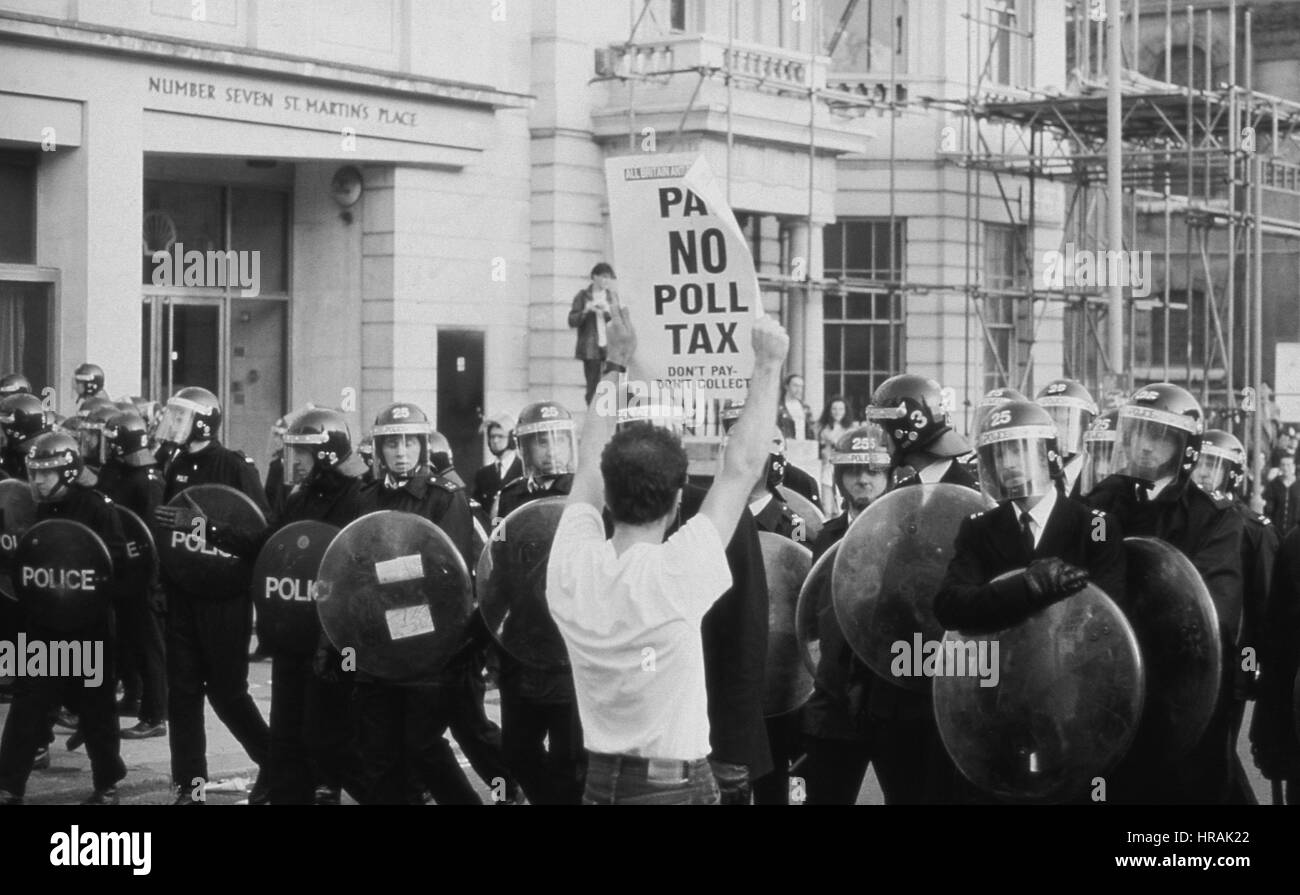 A protestor holds up a placard to a line of riot police during the Poll Tax Riots in London, England on March 31, 1990. The unpopular tax was introduced by the Conservative government led by Prime Minister Margaret Thatcher. Stock Photo