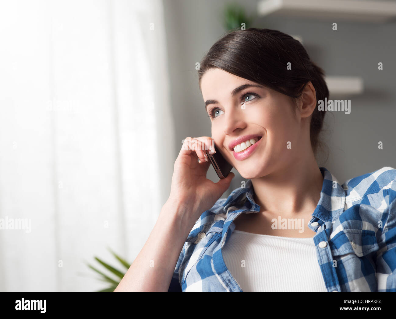 Smiling woman sitting on sofa in the living room having a phone call ...