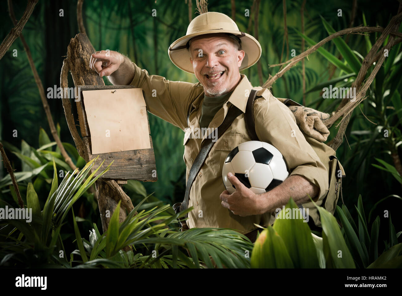 Smiling explorer in the jungle holding a soccer ball leaning to a sign. Stock Photo