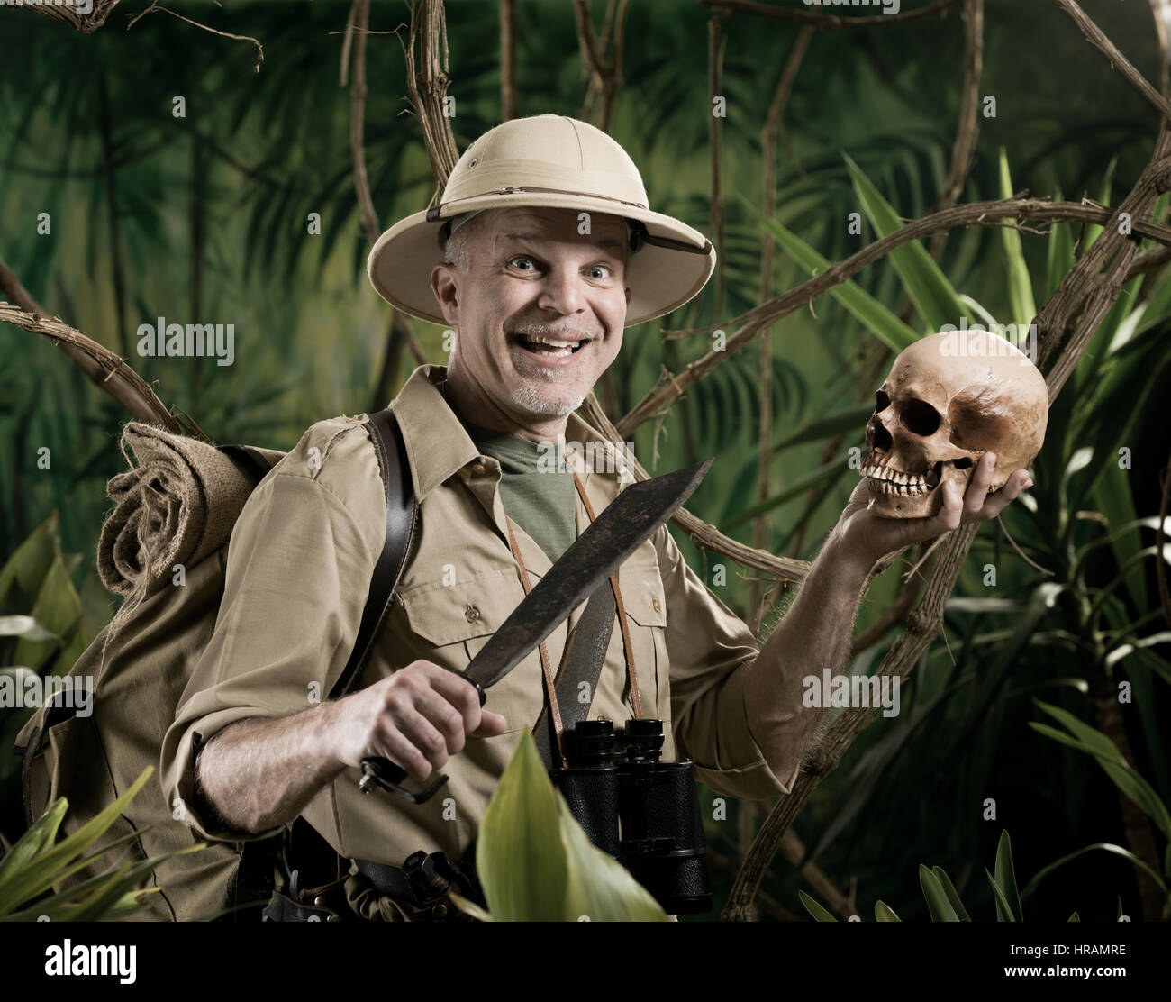 Smiling explorer in the jungle holding skull and machete. Stock Photo