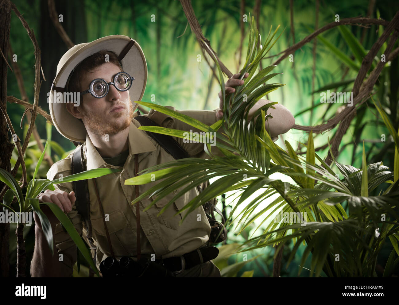 Young explorer guy walking in the rainforest jungle with exploration equipment and thick glasses. Stock Photo