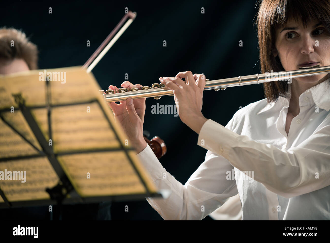 Professional female flutist performing on stage with sheet music Stock
